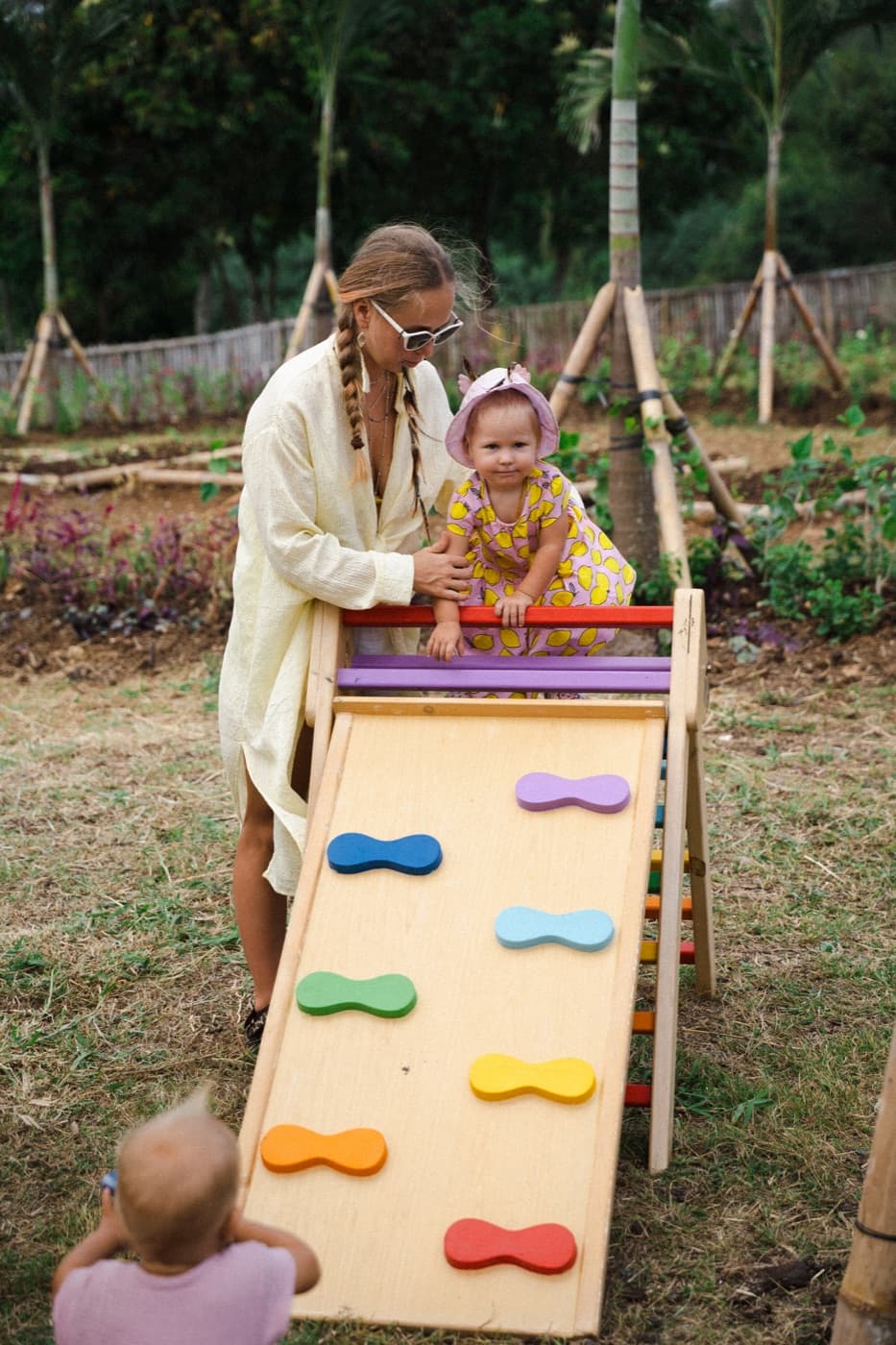 A toddler climbing a rainbow play ramp with a carer